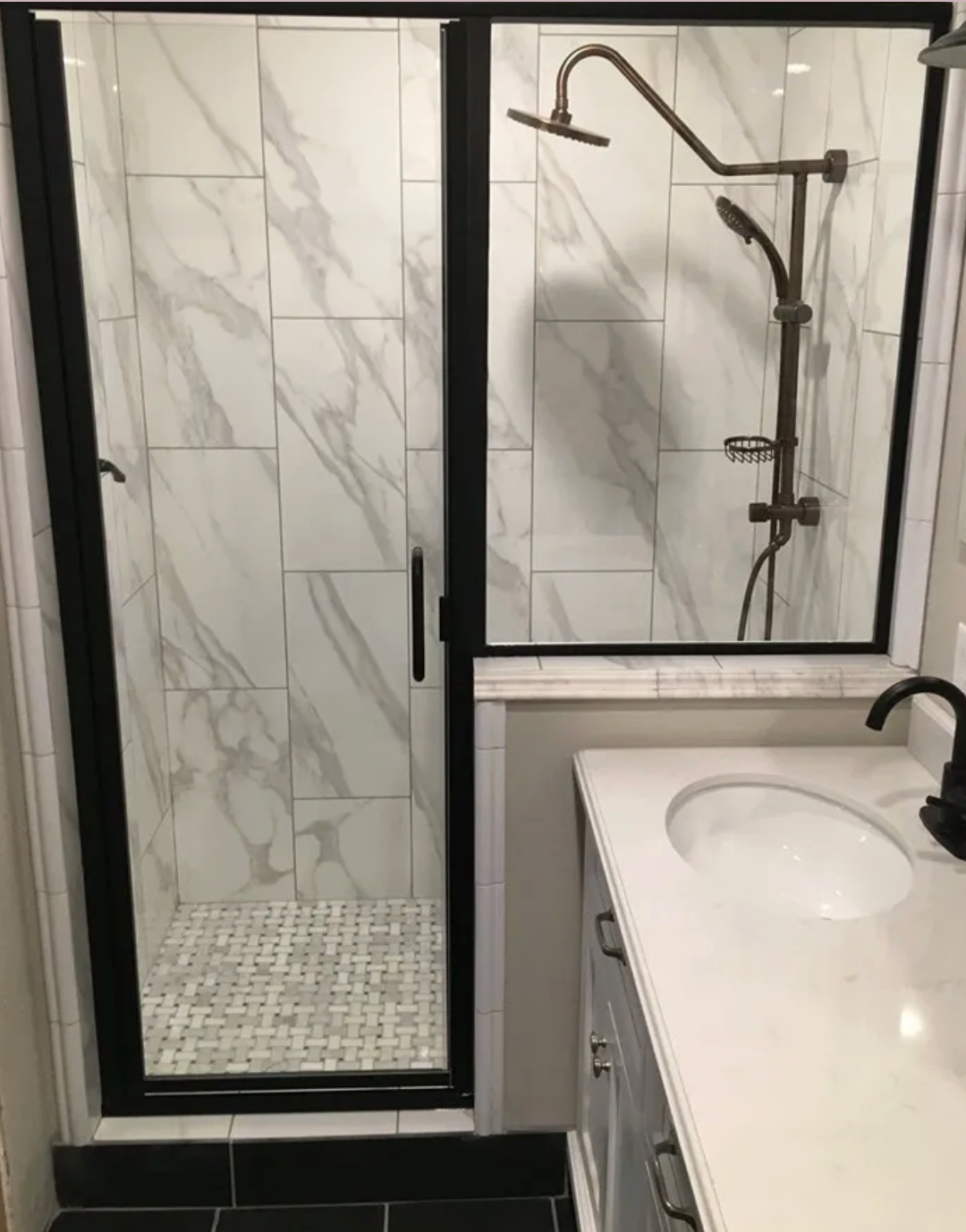 Shower with black frame, marble-look tile, brass shower fixtures, and white countertop vanity.