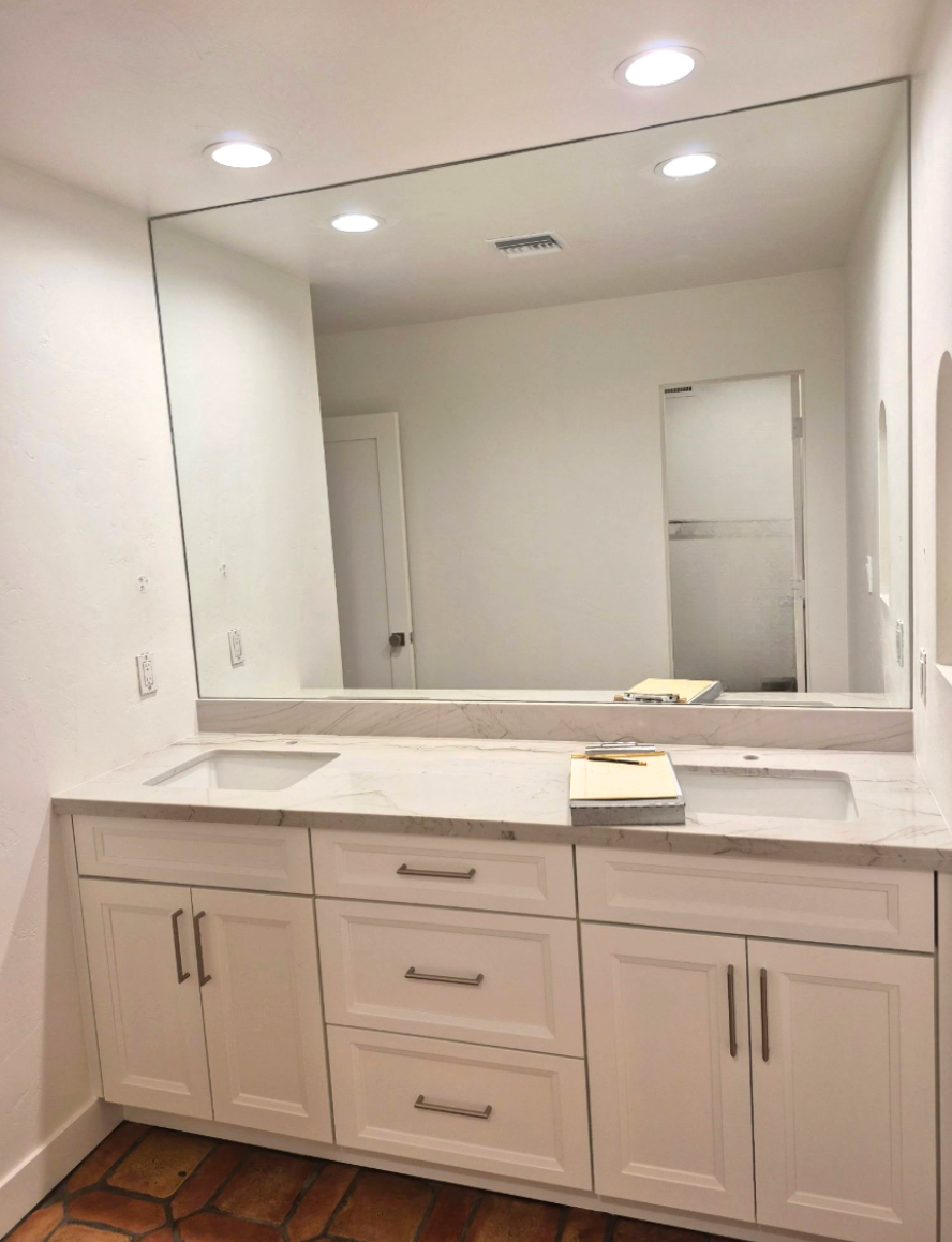 Bathroom with white cabinets, mirror, and a person taking a photo in the mirror.