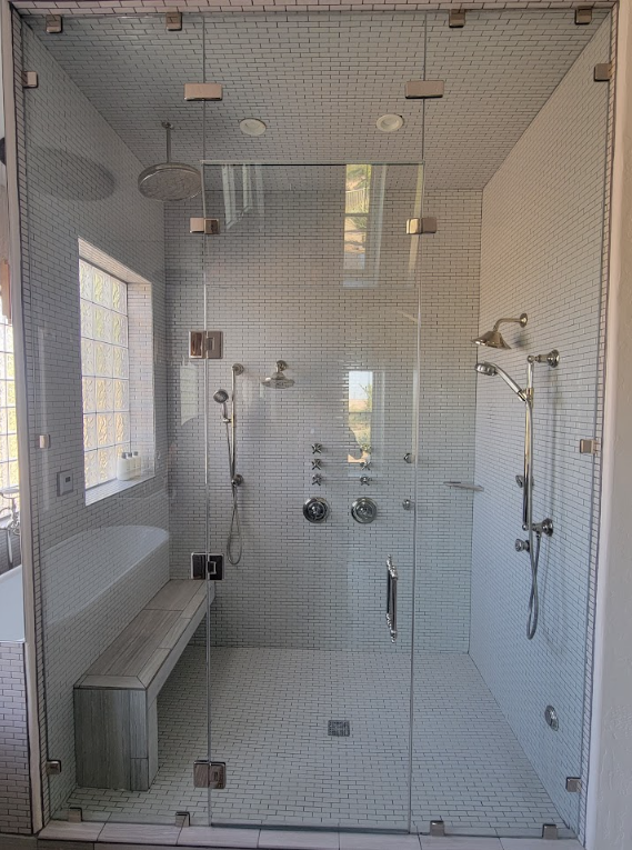 Glass-enclosed white tiled shower with multiple showerheads and a built-in bench