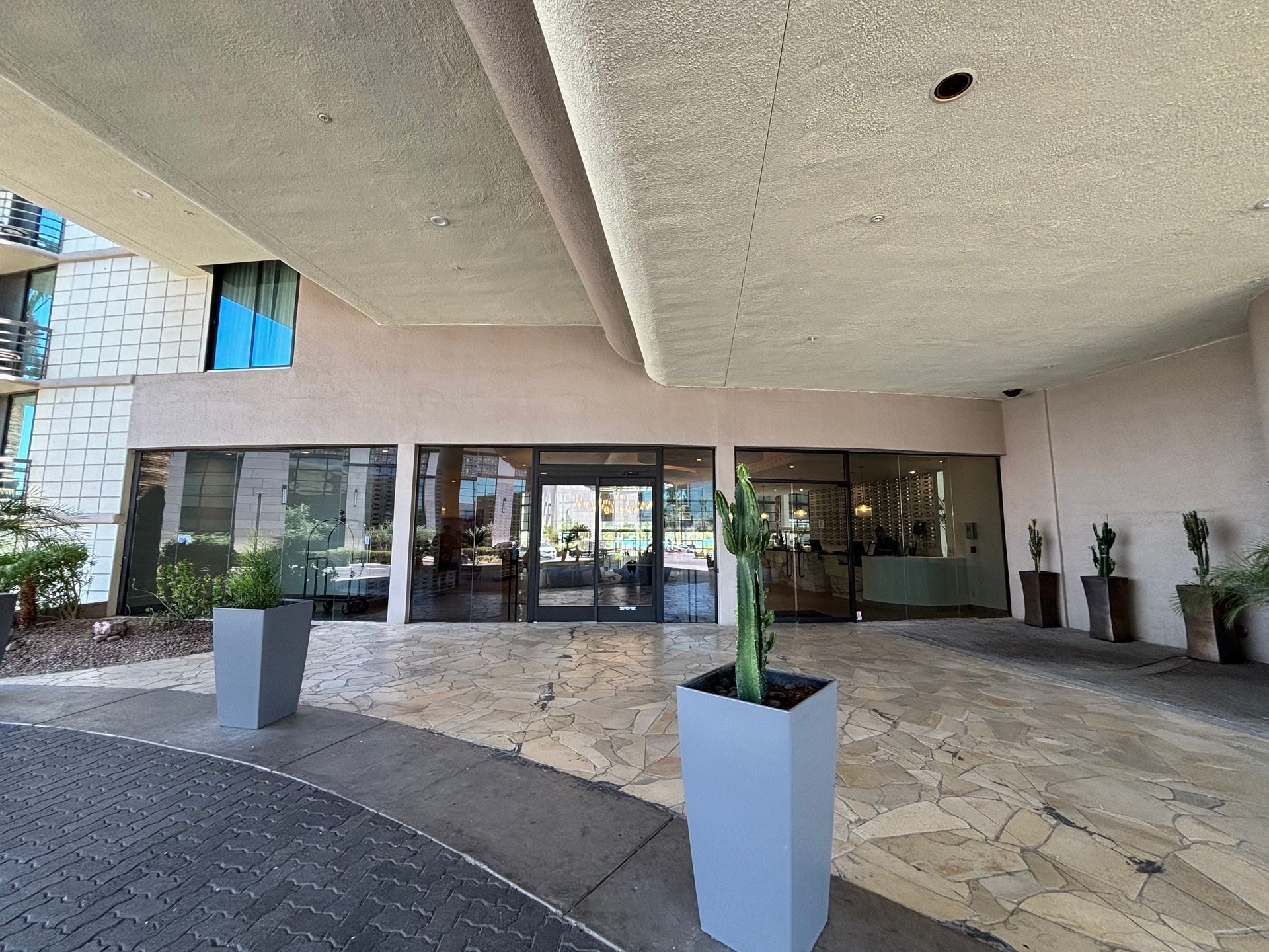 Entrance to a building with large glass doors, potted cacti, and a curved walkway.