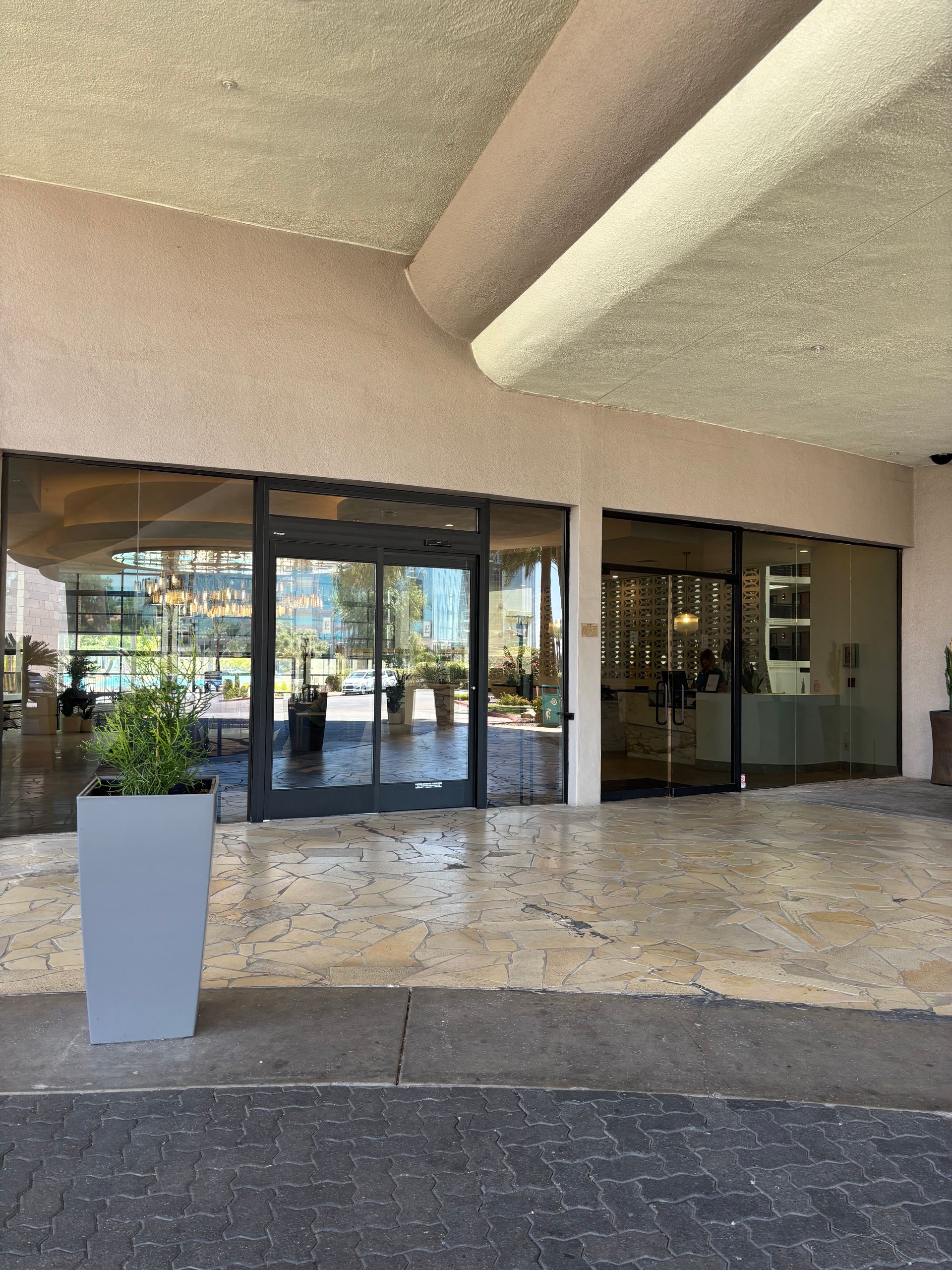 Entrance to a building with glass doors, stone paving, and a decorative planter.