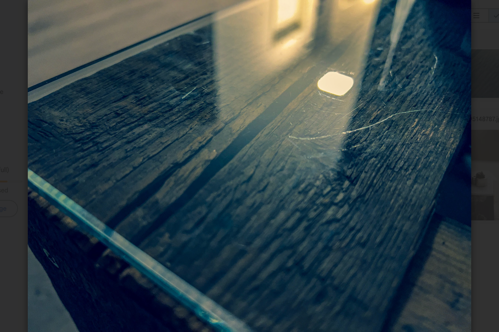 Glass-topped table with weathered wooden base. Reflective surface with sunlight and scratches.
