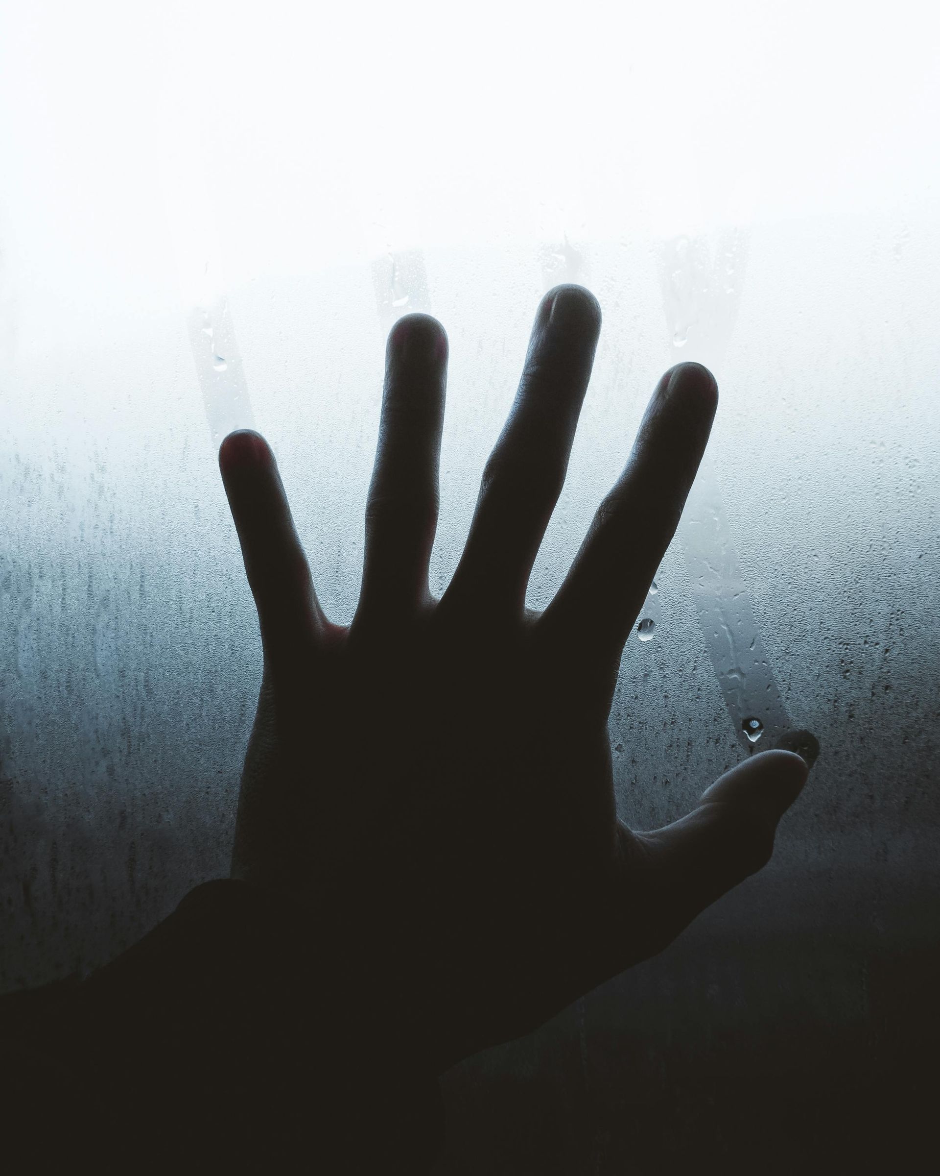 Silhouette of a hand pressed against a foggy window, fingers spread.