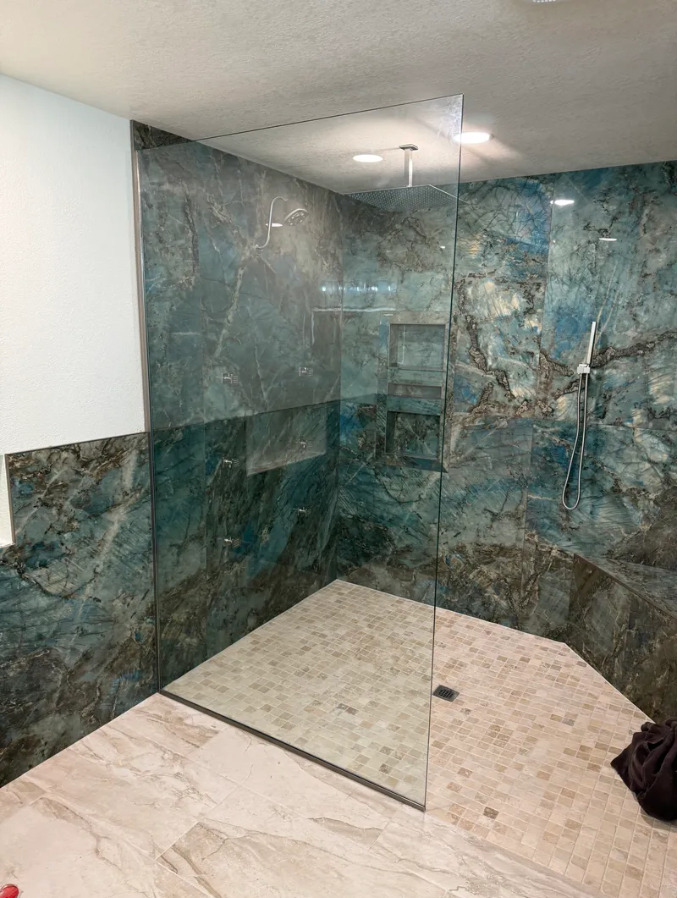 A walk-in shower with turquoise marble walls, glass panel, and beige tiled floor.