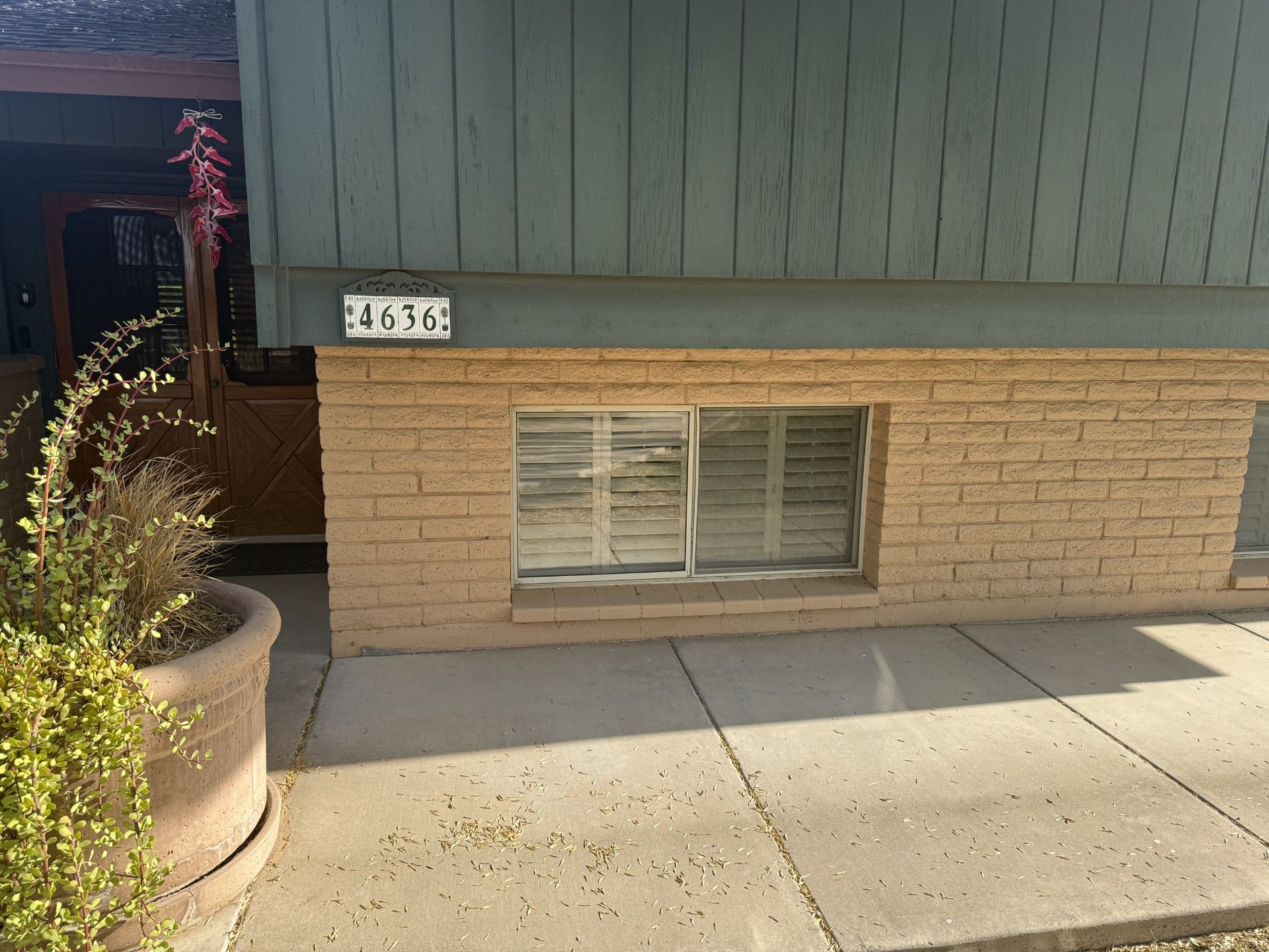 Exterior of a house with a pale brick facade, green siding, and address 4650 above a window with blinds.