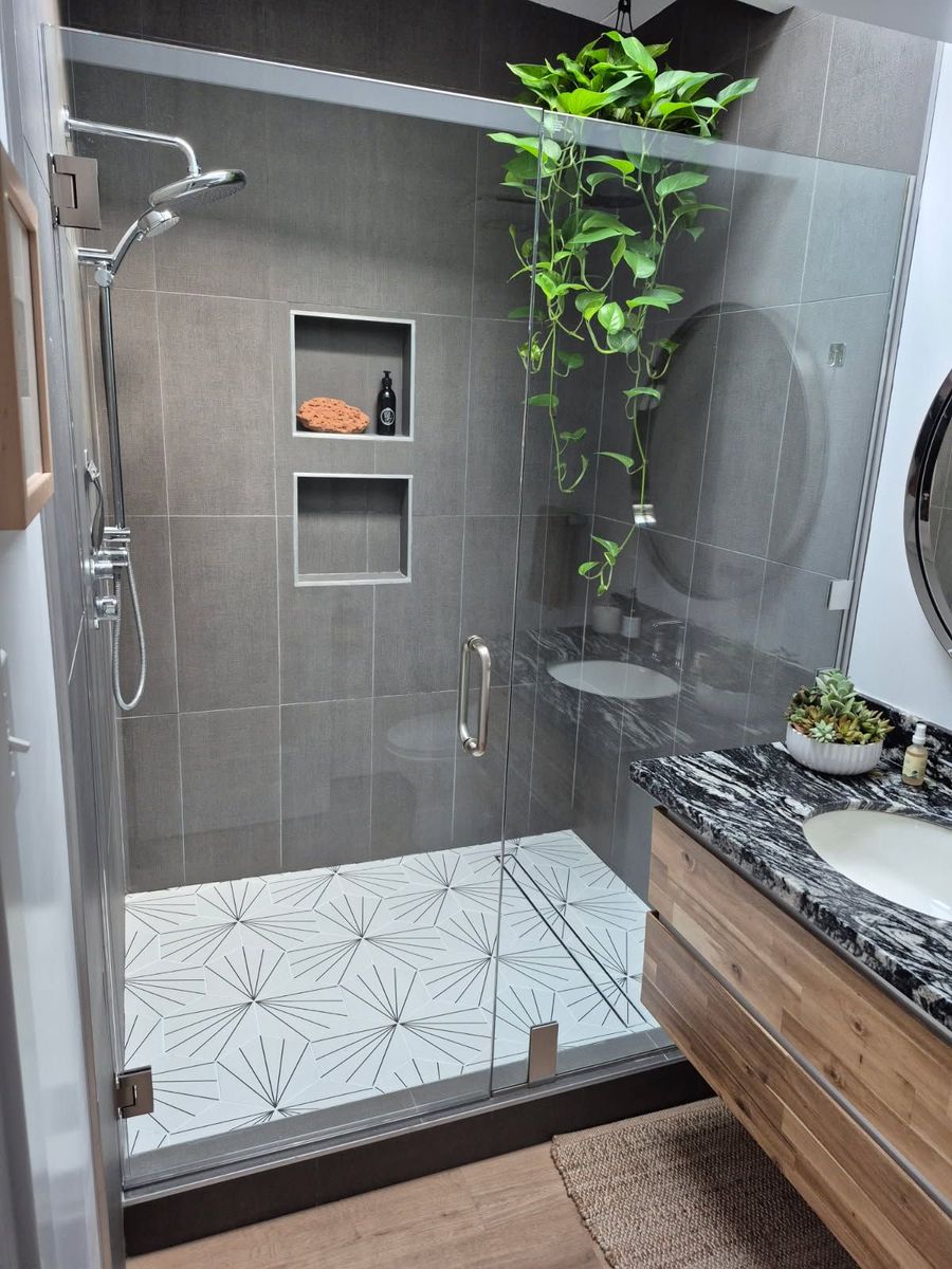 Shower with black frame and floral wallpaper, gray tile, and a small window.