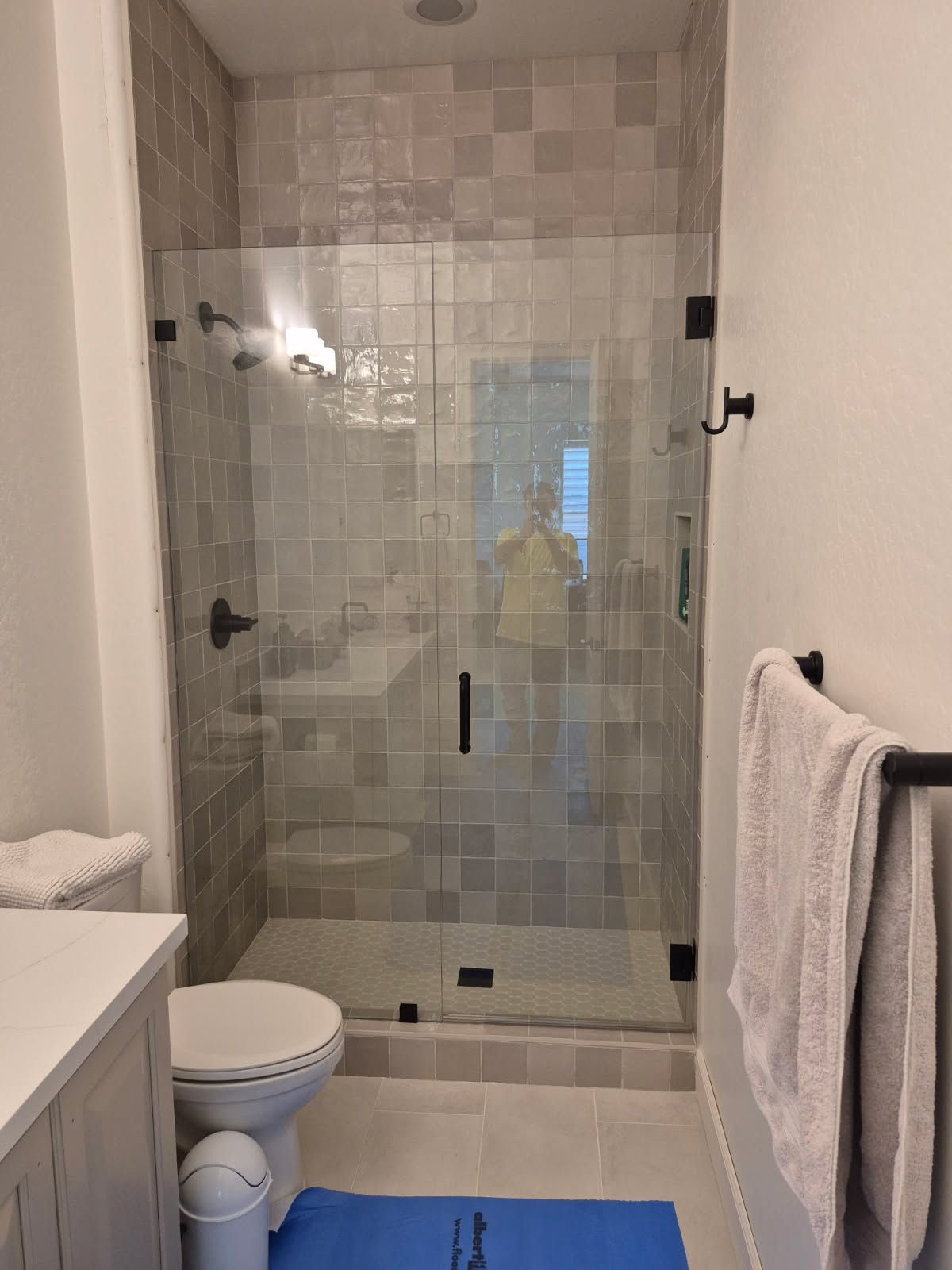 Modern bathroom with glass shower, toilet, white towels, and blue bath mat