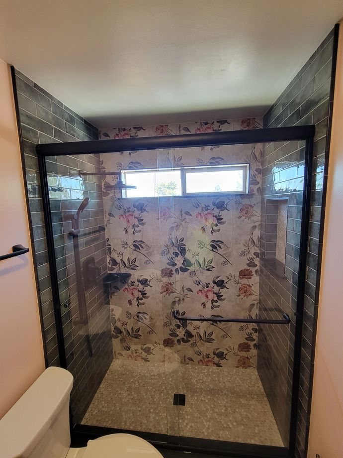 Shower with black frame and floral wallpaper, gray tile, and a small window.
