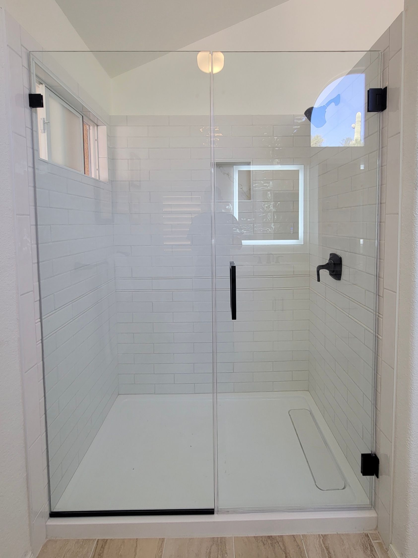 A modern, glass shower with black hardware and white tile.