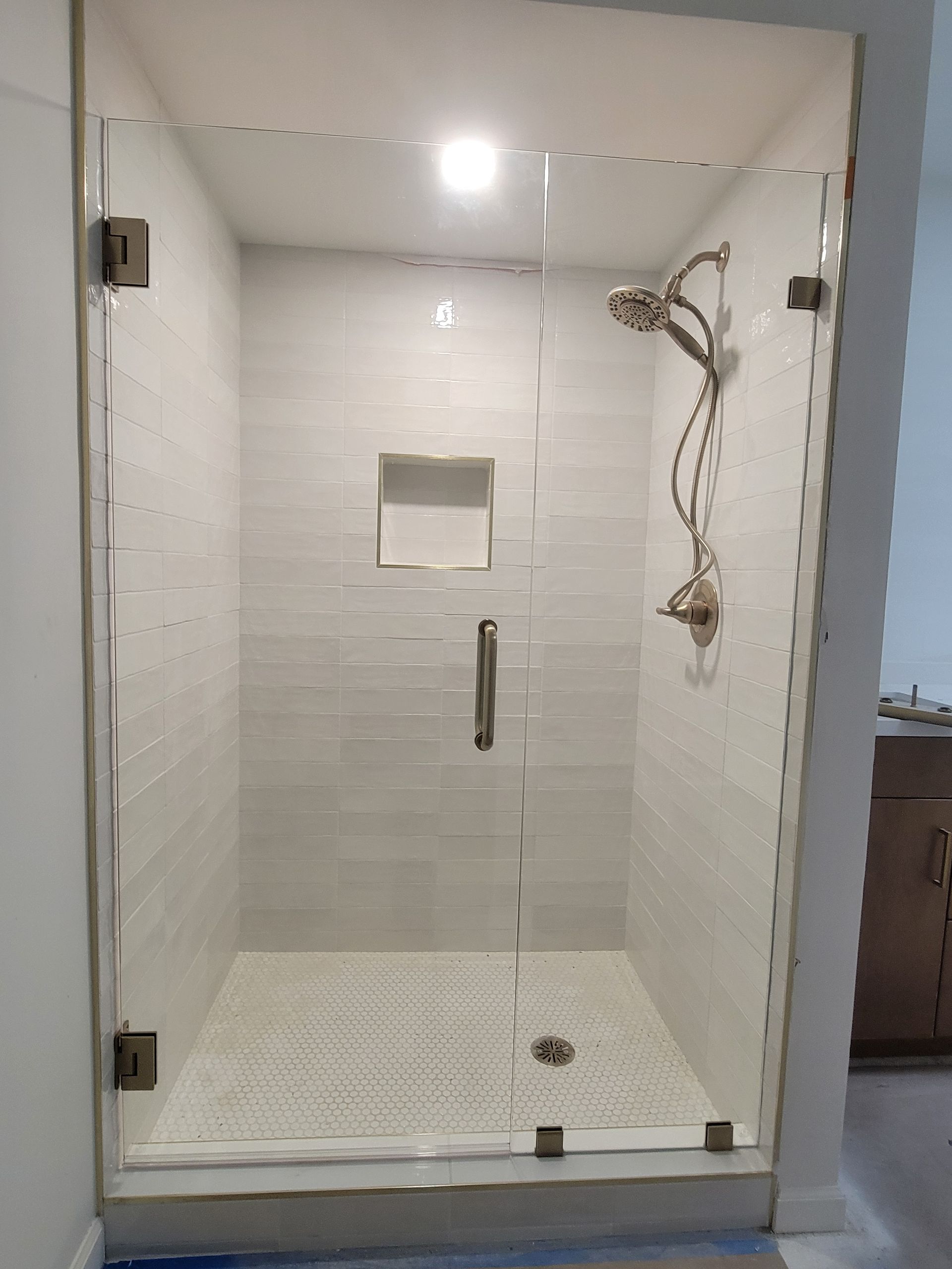Glass shower enclosure with white tile walls and mosaic floor. Bronze fixtures.