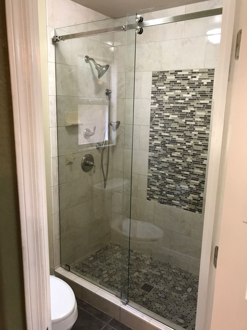 Shower with sliding glass doors, gray stone floor, tiled walls, and a mosaic accent.