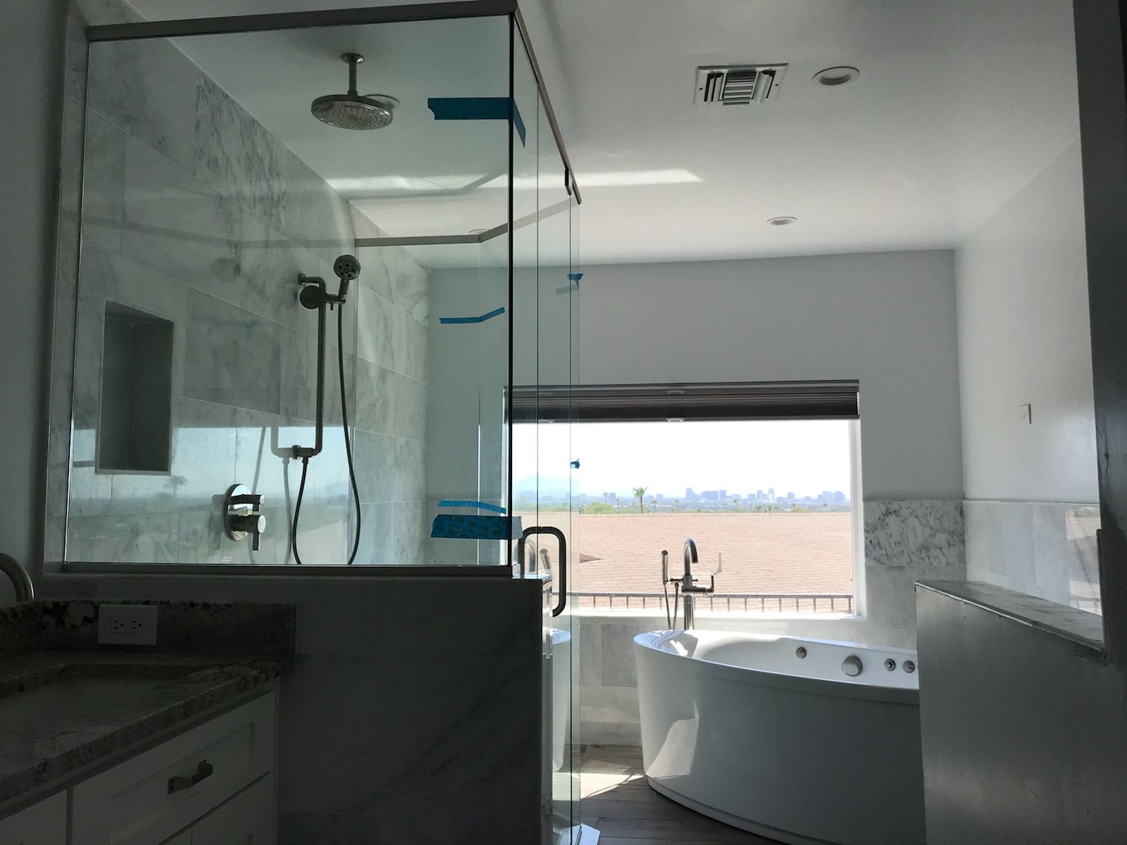 Modern bathroom with glass shower, jacuzzi tub, and window view.