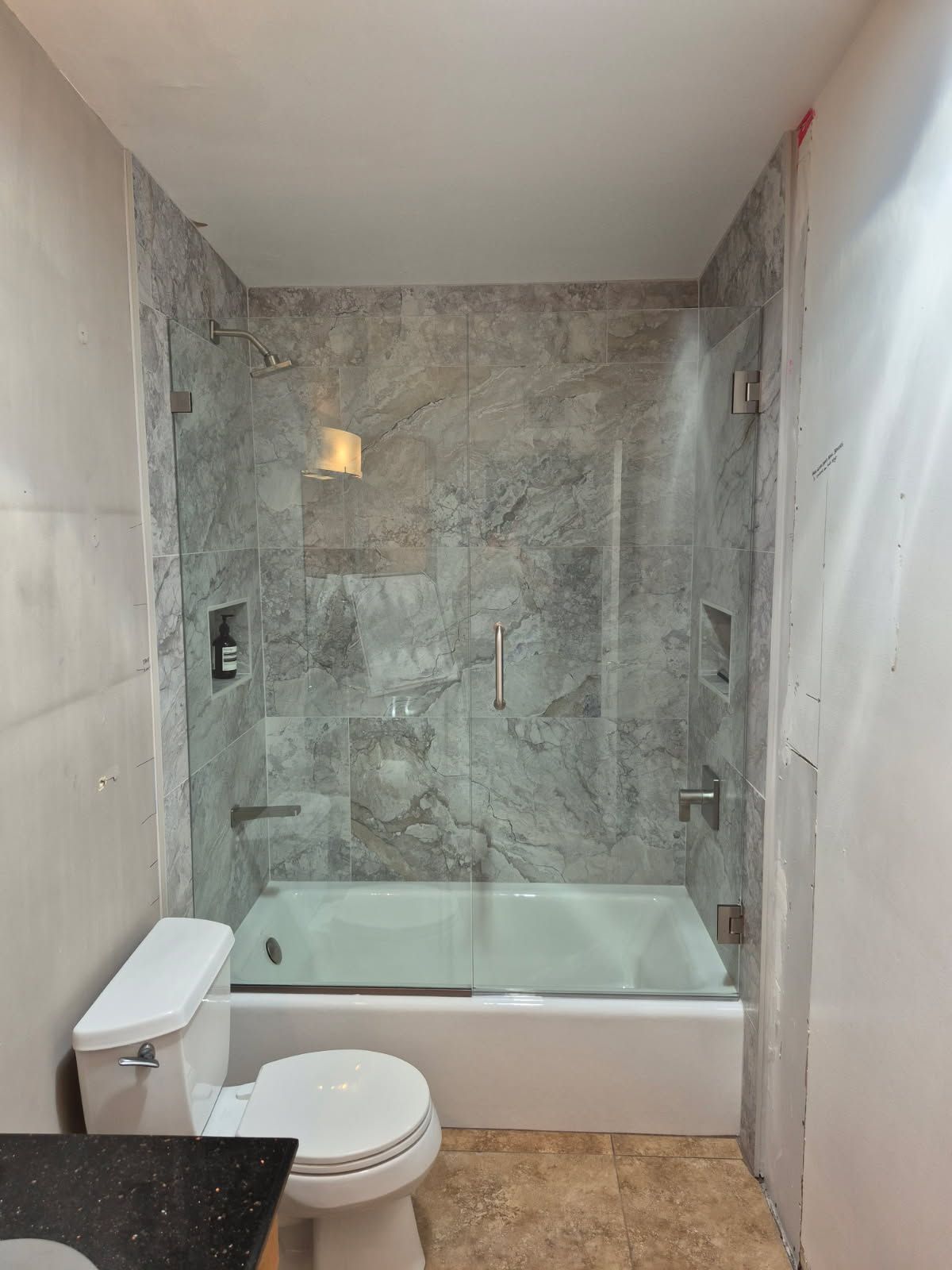 Bathroom with a white tub and glass shower doors, gray marble tile, and a white toilet.