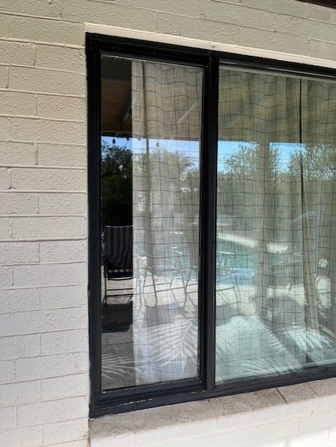 A shower with floral wallpaper inside, black framed glass doors and tiled exterior, next to a pink wall.