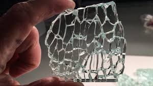 Hand holding a piece of shattered glass; the glass is clear, with a network of fractures.