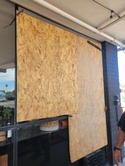 Large plywood sheets covering a store front window.  Black metal frame and support.  Outdoor setting, daylight.