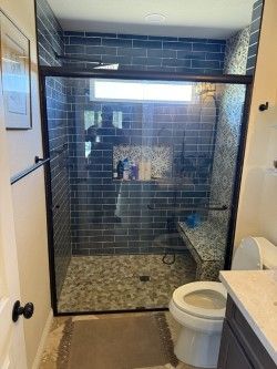 Bathroom with dark gray tile shower, pebble floor, glass door, and granite bench.