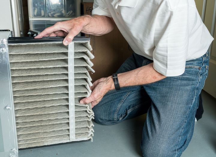 A man is kneeling down and cleaning an air filter.