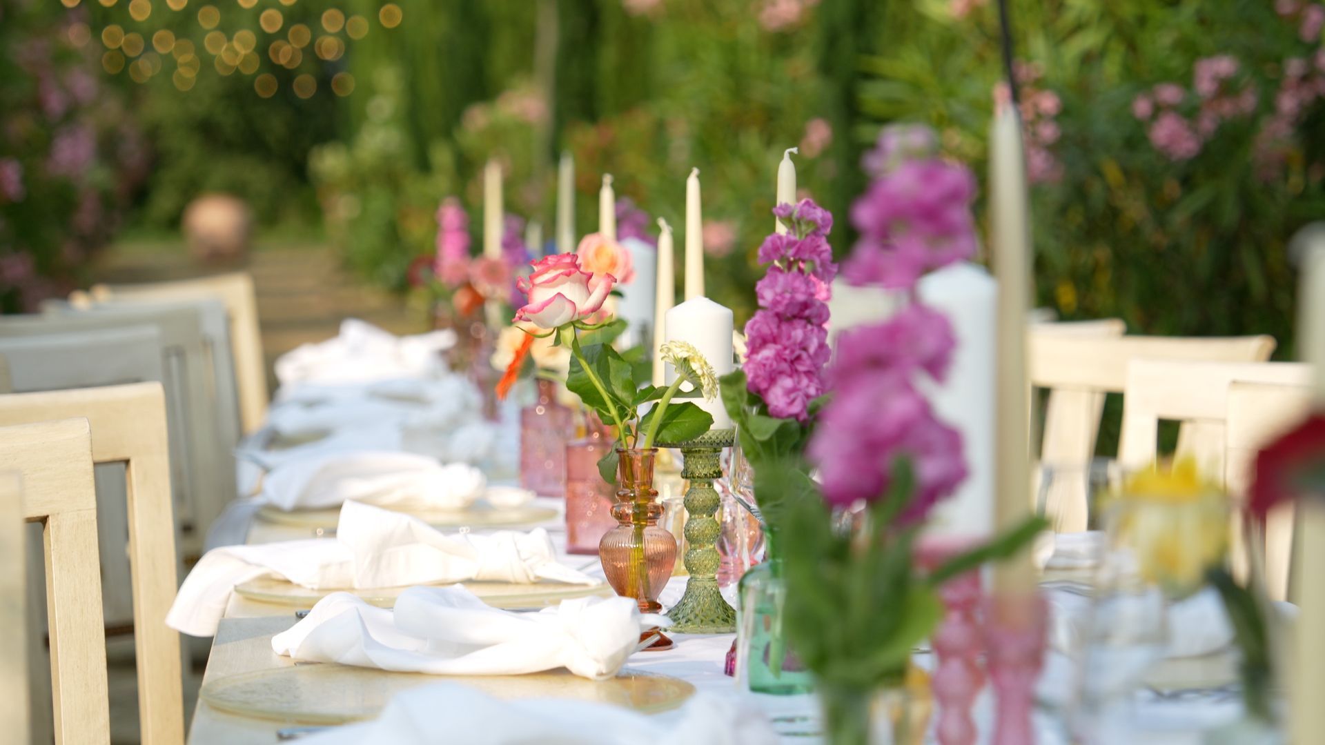Tavolo all'aperto apparecchiato per una cena formale, con tovaglie bianche, candele e fiori rosa