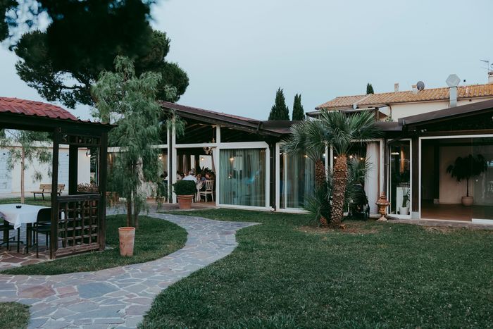 Giardino interno con sentiero in pietra, gazebo e patio con vetrata, all'ombra degli alberi al crepuscolo.