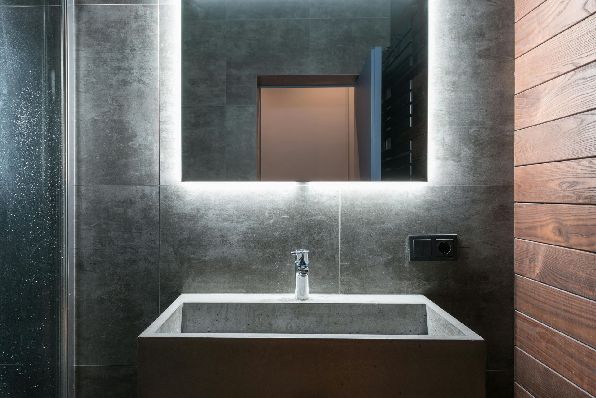 Bathroom with gray concrete sink, backlit mirror, and wooden paneling.