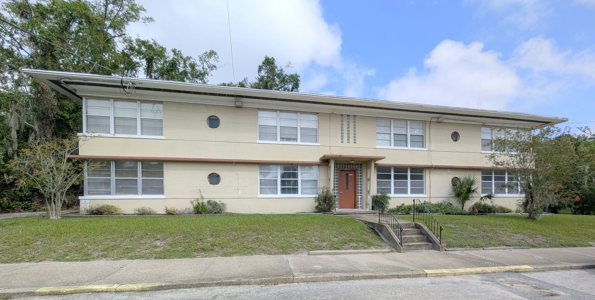Two-story apartment building with tan facade, white trim, and grassy lawn.