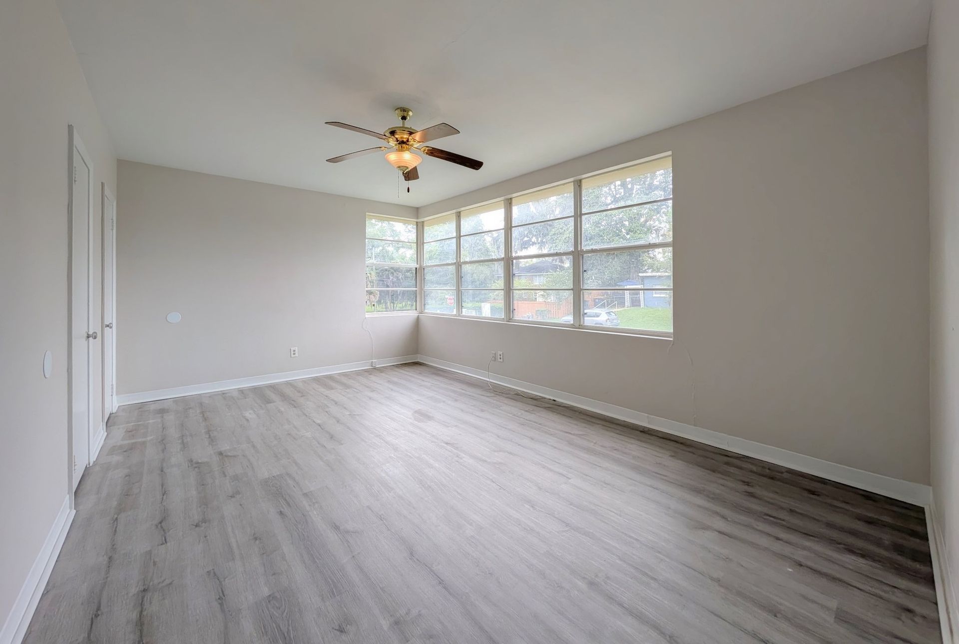 Empty room with gray wood-look flooring, multiple windows, ceiling fan, and white walls.