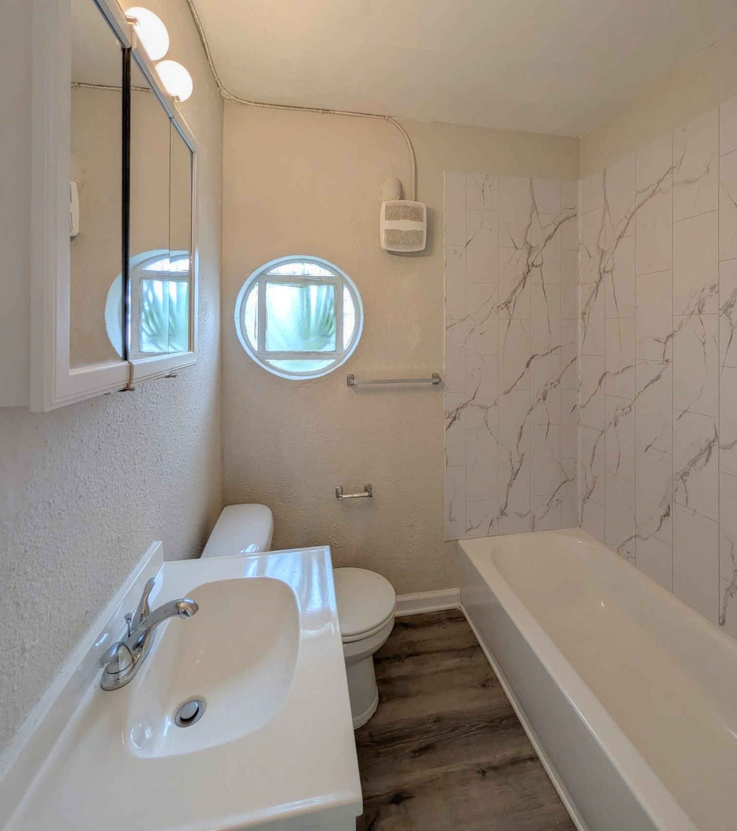 Bathroom with sink, toilet, tub, round window, and faux marble wall.