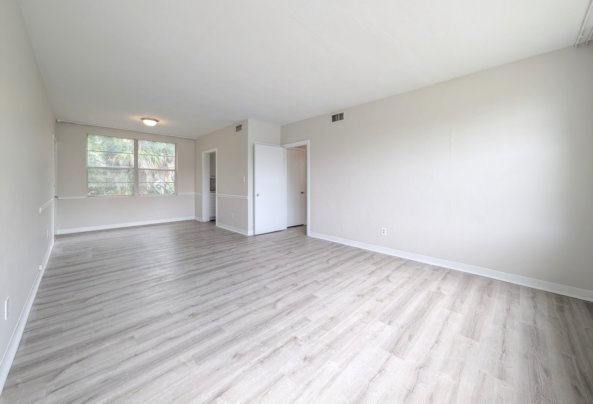 Empty living room with light grey walls, light wood-look flooring, and a window.