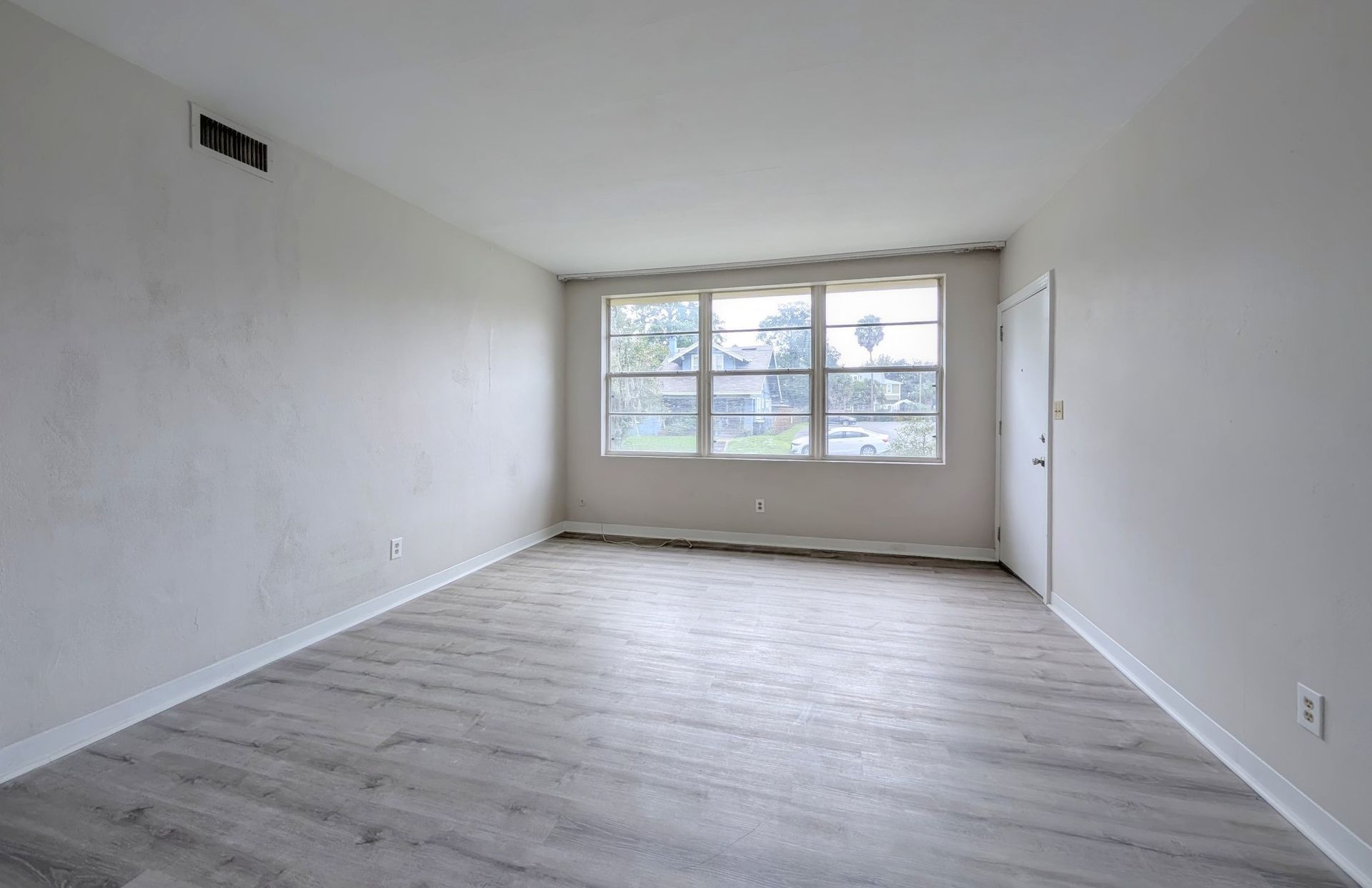 Empty room with gray wood-look flooring, white walls, window, and door.