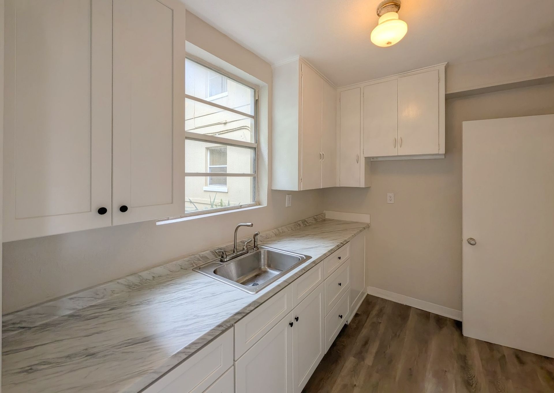 White kitchen cabinets and countertops with a window, sink, and door.