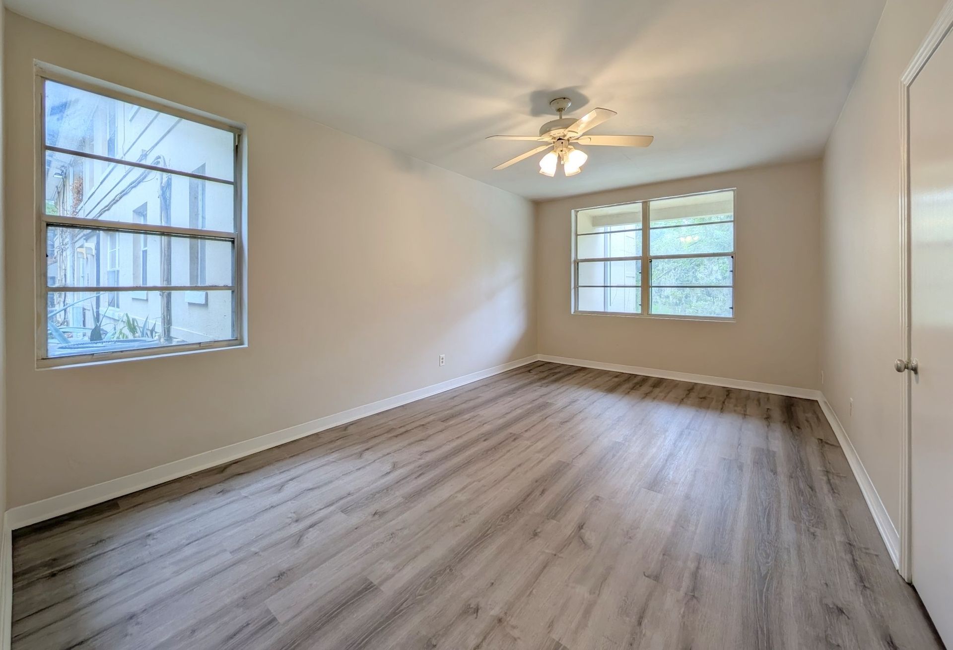 Empty bedroom with light wood-look flooring, two windows, ceiling fan, and white walls.