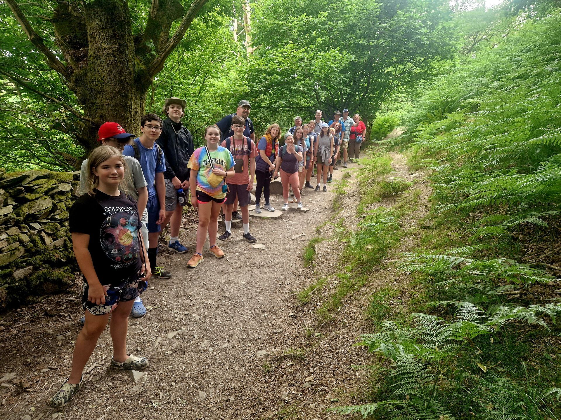 A group of children are standing on a dirt path in the woods