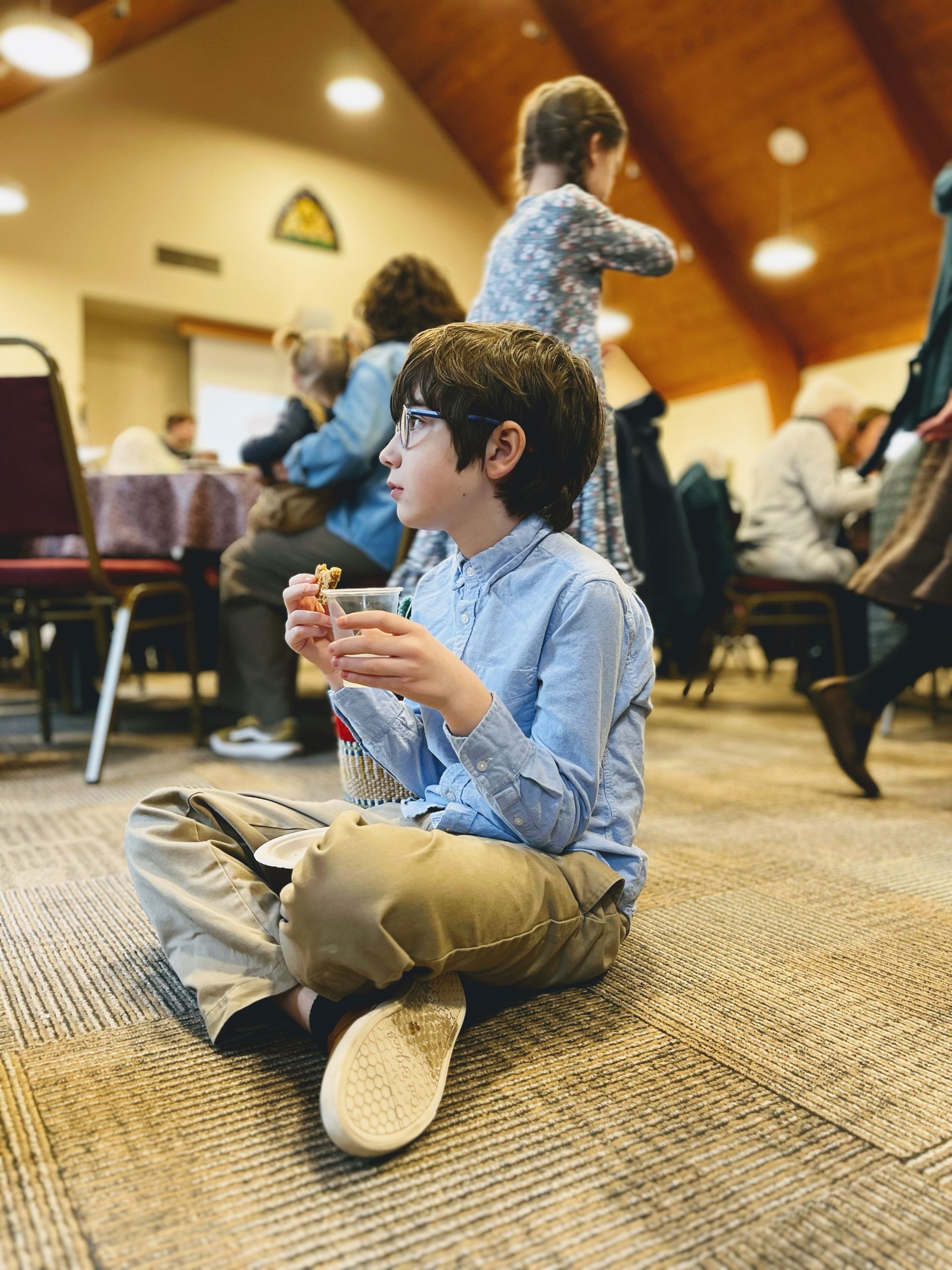 A young boy is sitting on the floor eating a snack