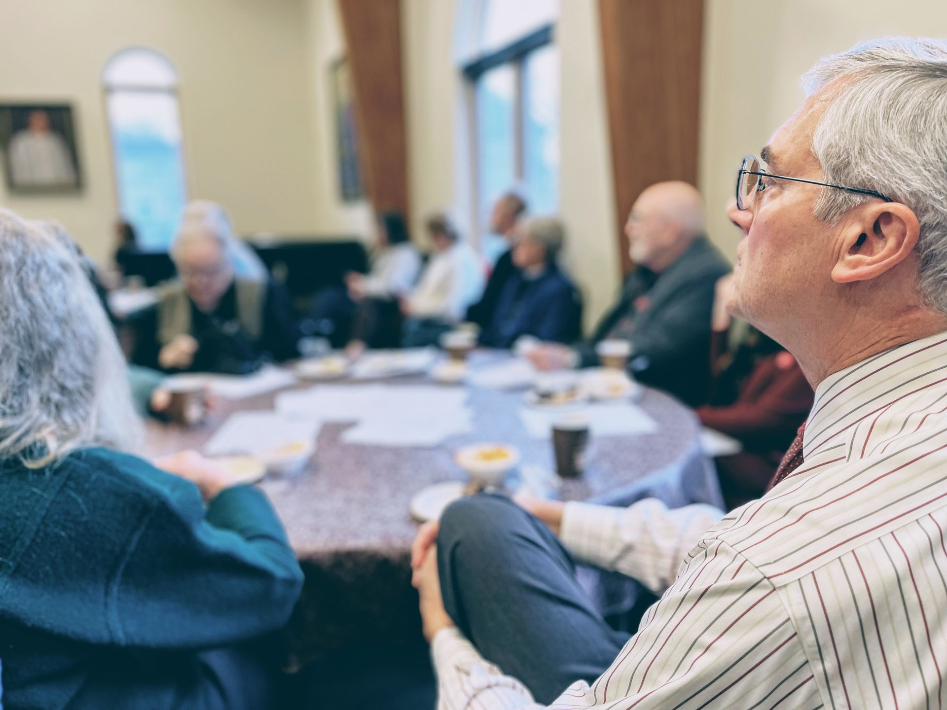 A man wearing glasses sits at a table with other people
