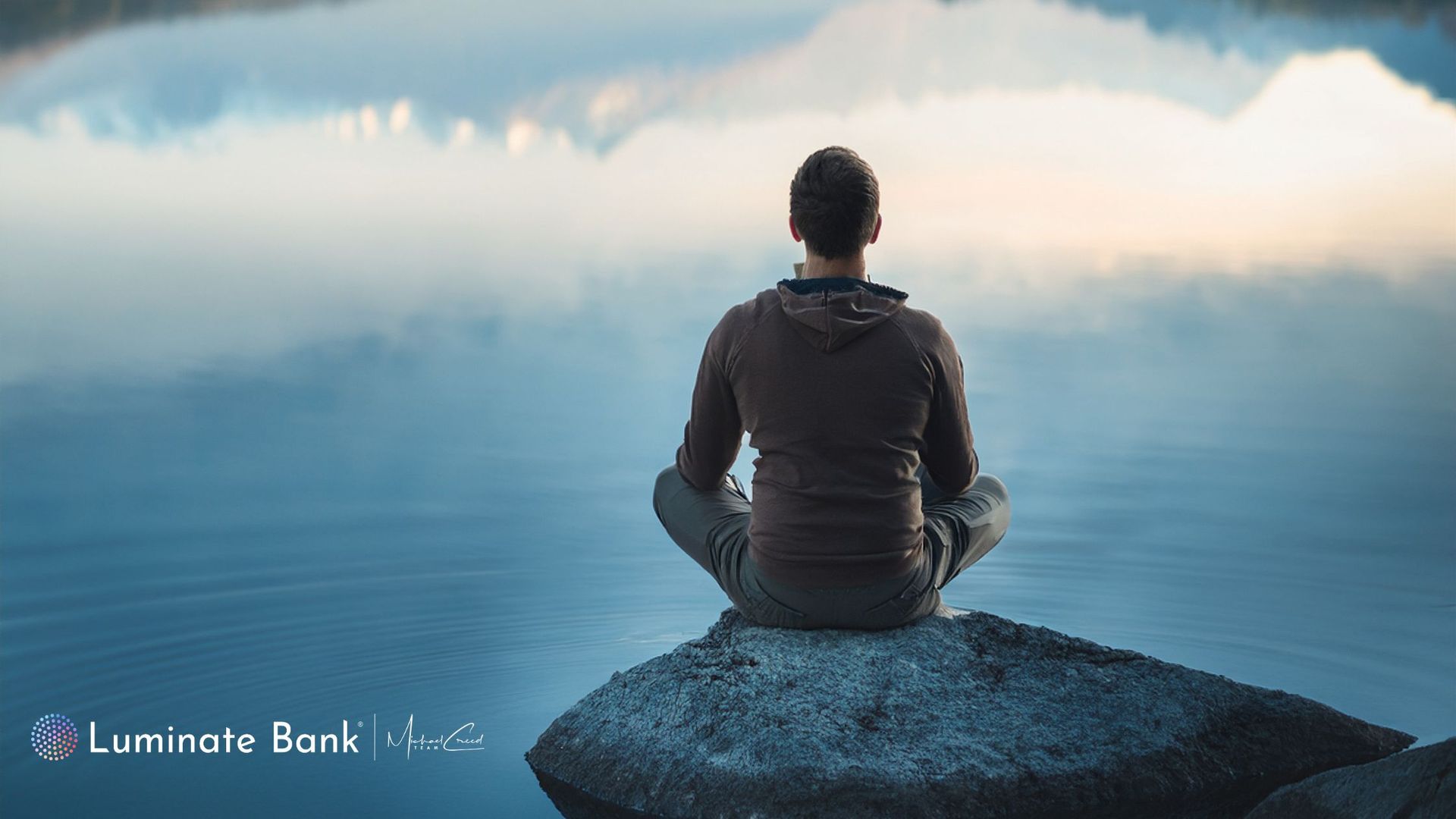 Man sitting on a rock in a lake reflecting. 