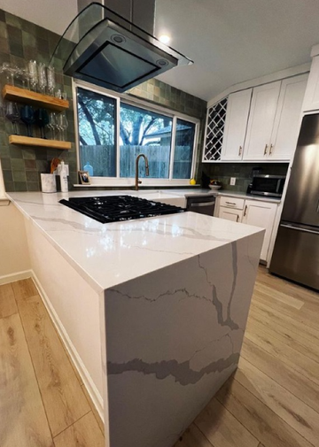 Modern kitchen with white island, marble surfaces, black cooktop, and stainless appliances