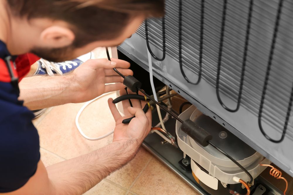 Man Repairing the Back of a Refrigerator With Tools, Focusing on Wires and Components — Industry Fire Services in Bowen, QLD