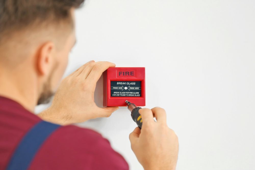 Person Installing or Checking a Red Fire Alarm on a White Wall — Industry Fire Services in Port Douglas, QLD