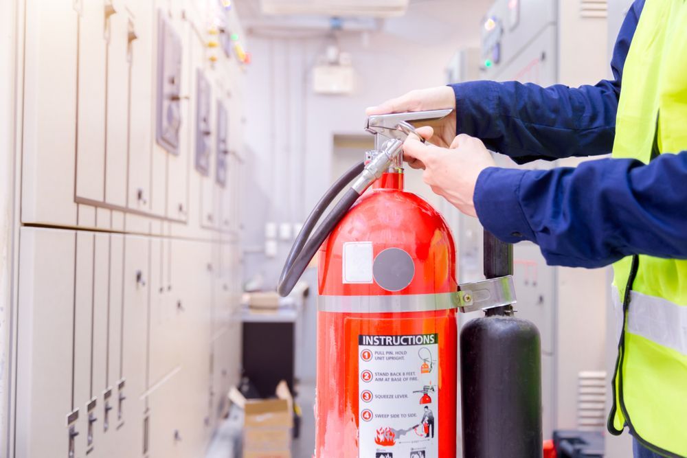 Person in a Yellow Vest Checks a Red Fire Extinguisher in an Electrical Room — Industry Fire Services in Bowen, QLD