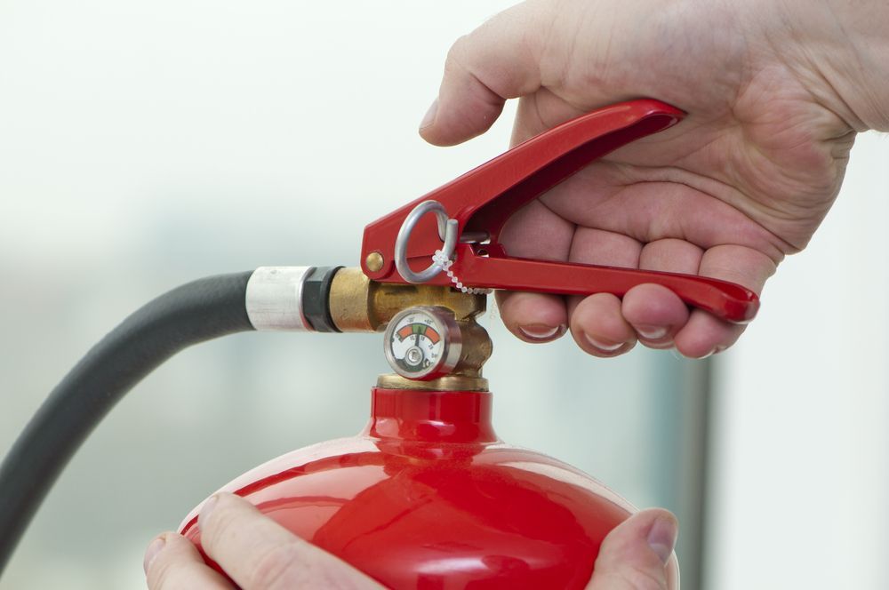 Person's Hands Activating a Red Fire Extinguisher, Pulling the Handle — Industry Fire Services in Ingham, QLD