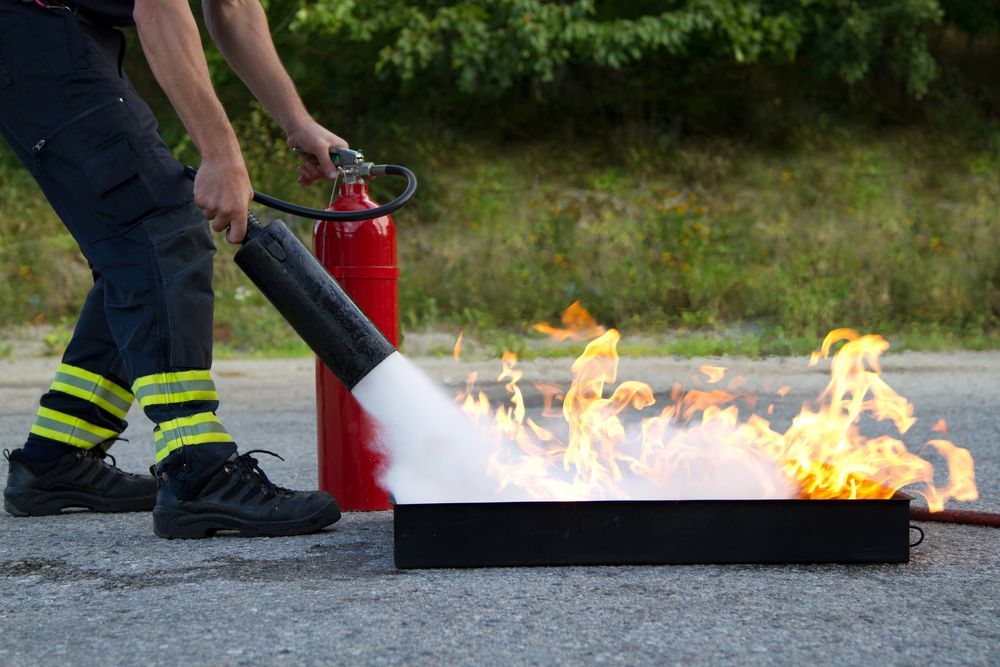Firefighter Extinguishing a Fire With a Fire Extinguisher on a Paved Surface — Industry Fire Services in Bowen, QLD