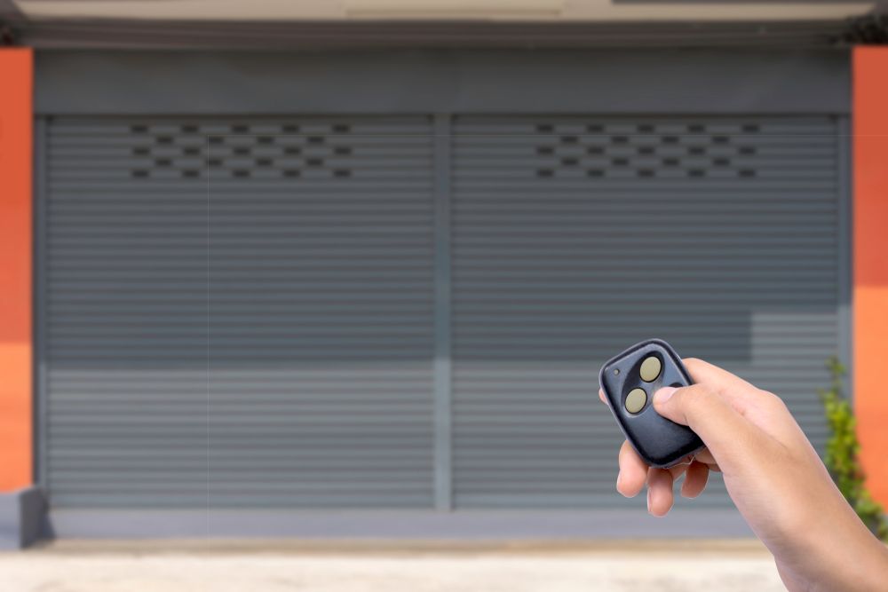 Hand Holding Remote, Opening Gray Metal Security Shutter Door — Industry Fire Services in Sunshine Coast, QLD