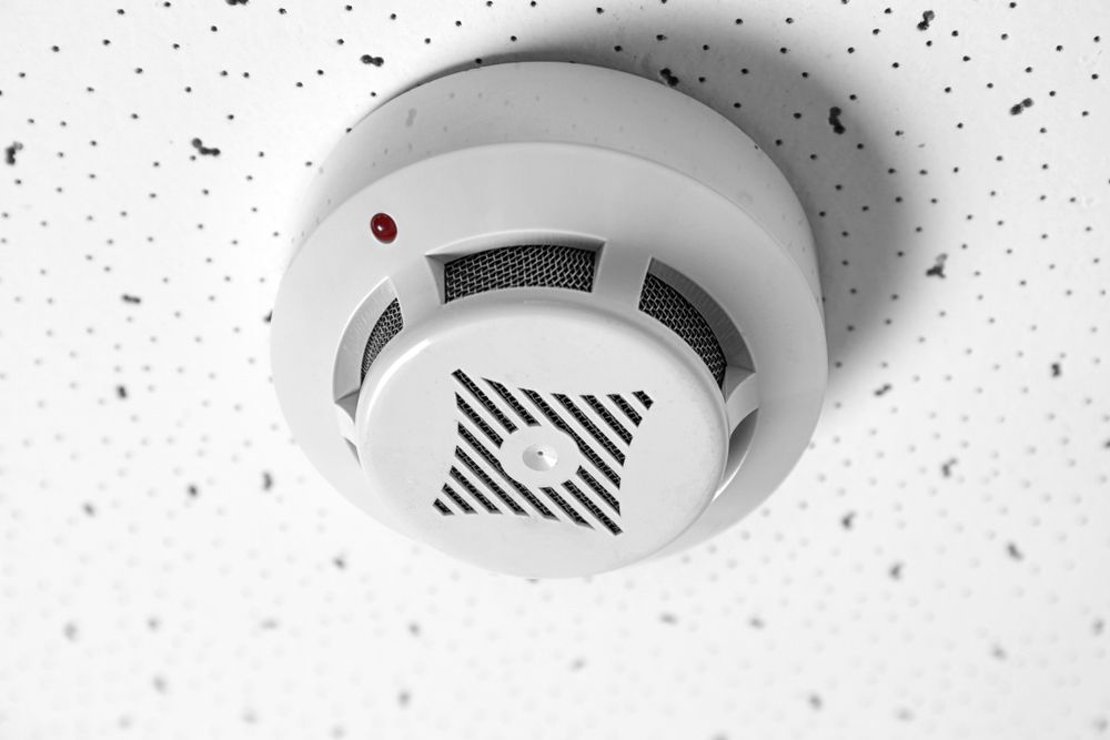 White Smoke Detector Mounted on a Textured Ceiling With a Red Indicator Light — Industry Fire Services in Mackay, QLD