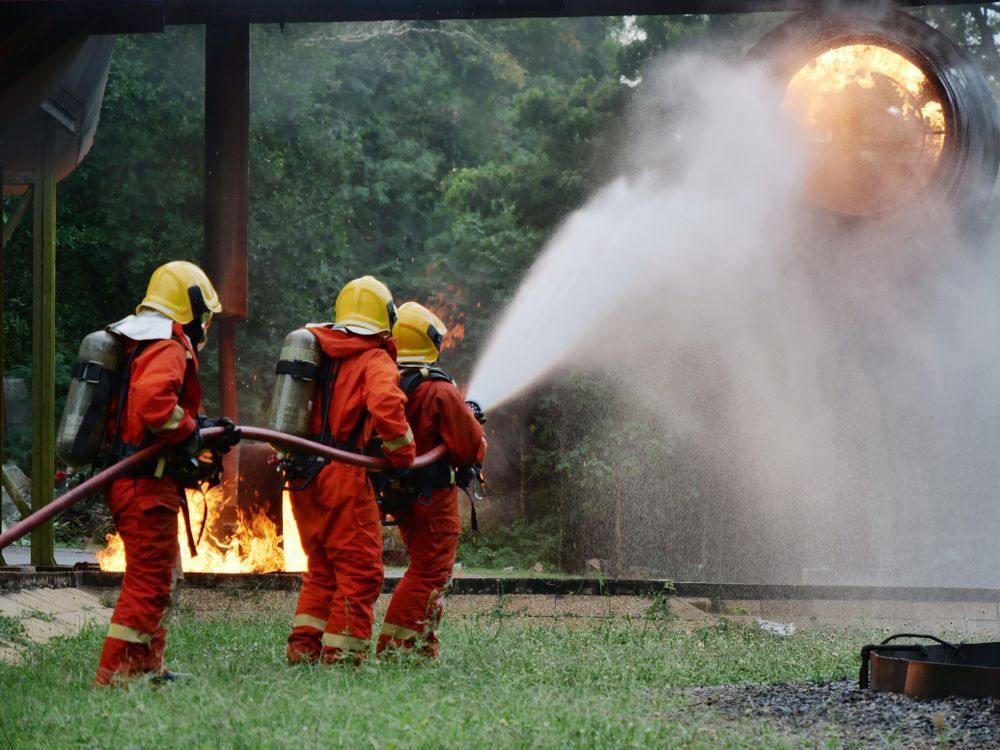 Firefighters in Orange Protective Gear Spray Water at a Fire During a Training — Industry Fire Services in Sunshine Coast, QLD