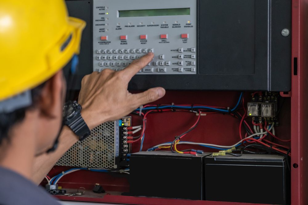 Person in a Yellow Hard Hat Presses a Button on a Fire Alarm Control Panel — Industry Fire Services in Toowoomba, QLD
