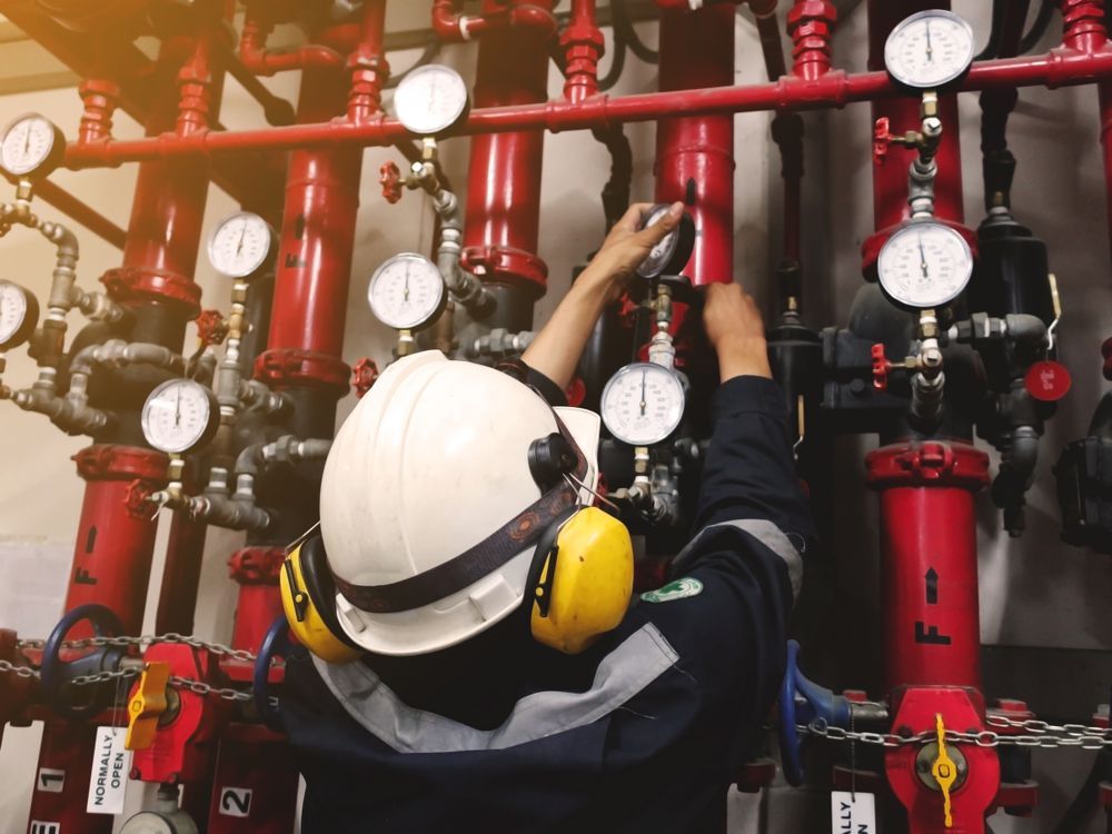 Person in a Hard Hat and Ear Protection Checks Gauges on Red Pipes — Industry Fire Services in Mount Isa, QLD