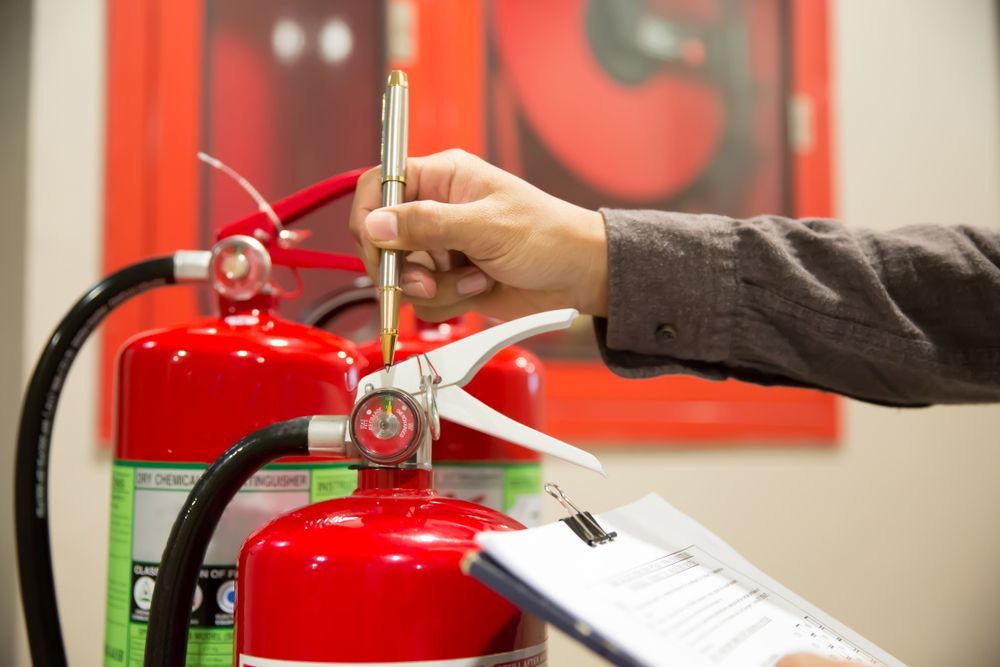 Person Inspecting Fire Extinguishers, Holding Pen and Clipboard — Industry Fire Services in Charters Towers, QLD