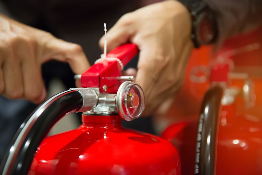 Person's Hands Activating a Red Fire Extinguisher, Pulling a Safety Pin — Industry Fire Services in Mount Isa, QLD