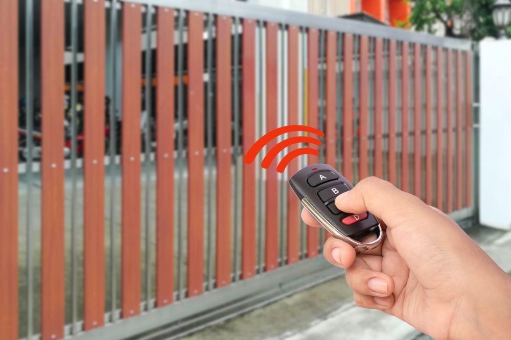 Hand With Remote, Activating a Brown and Silver Automatic Sliding Gate — Industry Fire Services in Mount Isa, QLD